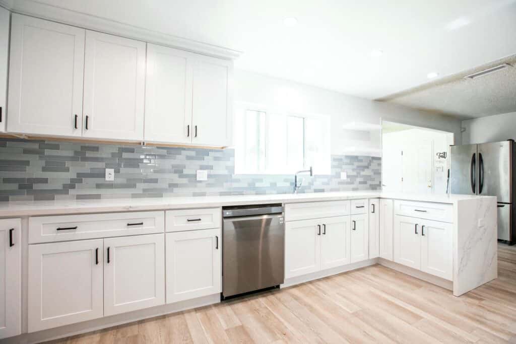 Altadena kitchen with white cabinets, a blue-gray backsplash and a bright window over the worktop